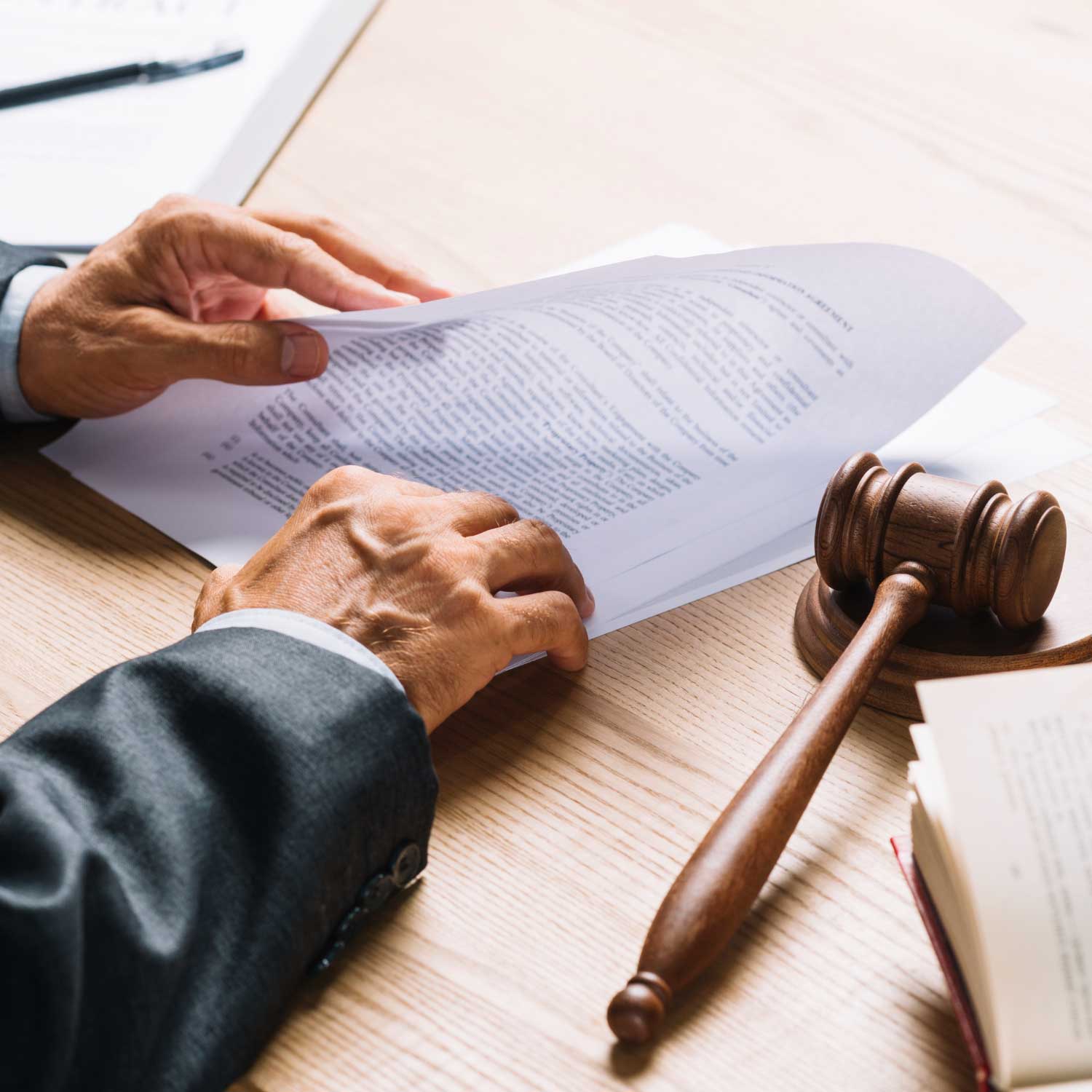 Una persona con traje revisa documentos en un escritorio con un mazo de madera y un libro abierto, lo que sugiere un entorno legal o de tribunal.